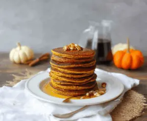 Delicious coconut flour pumpkin pancakes topped with maple syrup and garnished with fresh cinnamon, served on a white plate for a healthy breakfast.