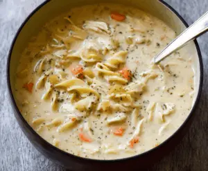Creamy chicken noodle soup in a bowl with tender chicken, vegetables, and noodles, topped with fresh herbs for a comforting and hearty meal