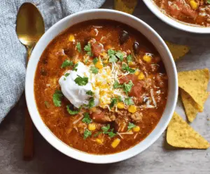 Delicious Slow Cooker Taco Soup in a bowl topped with shredded cheese, fresh cilantro, and sour cream, served with tortilla chips